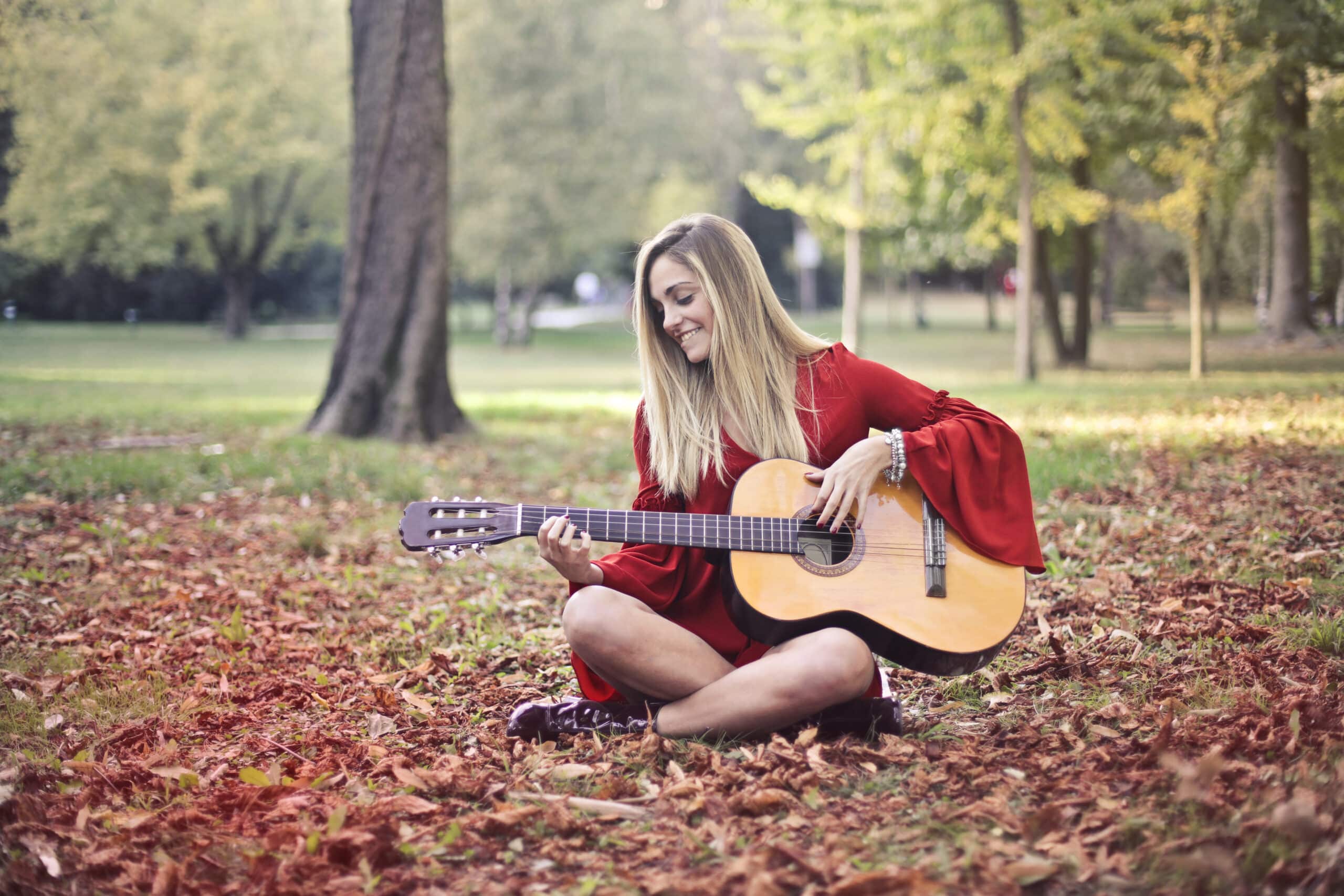 Woman in red long sleeve dress playing brown acoustic guitar sitting on the ground